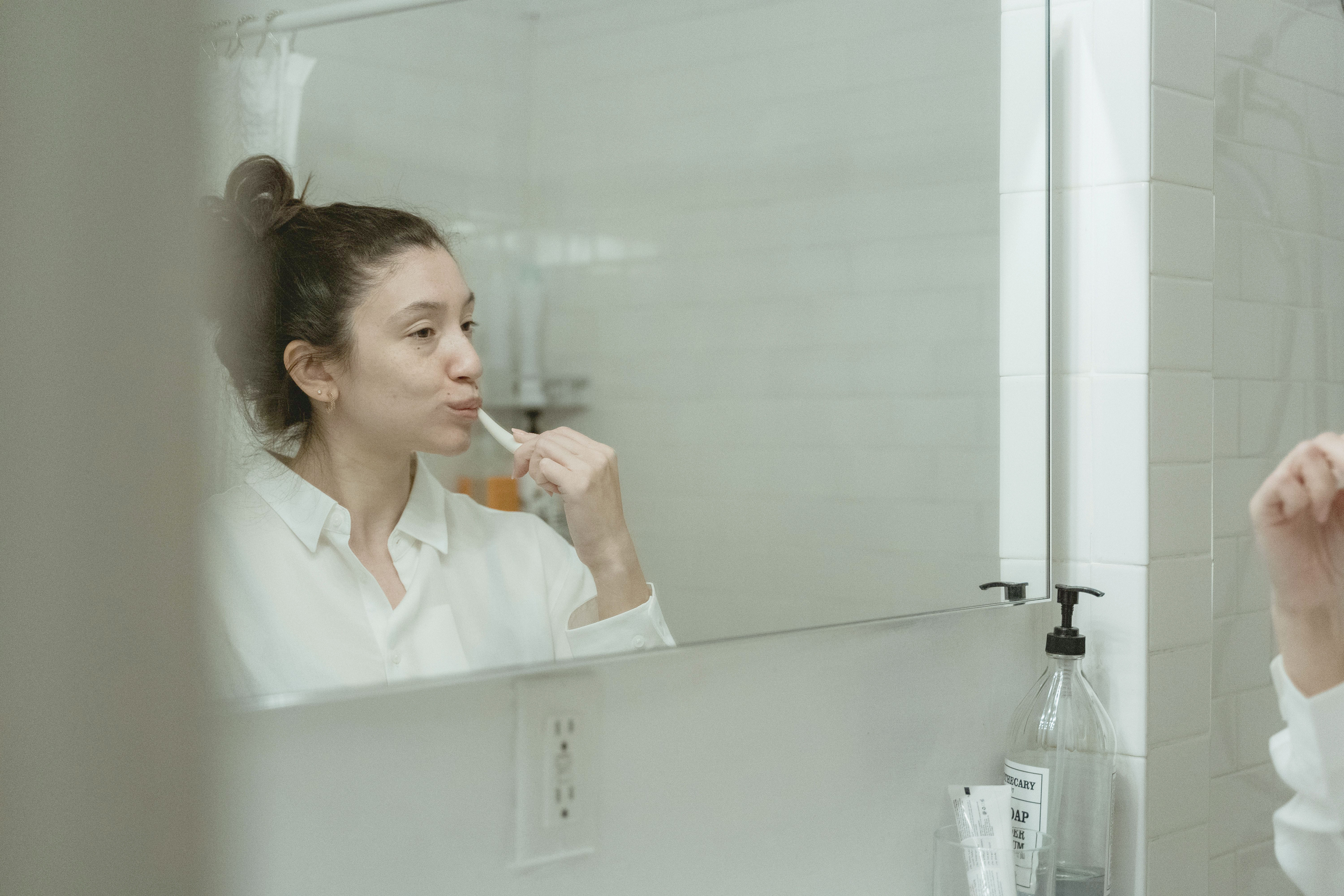Person brushing their teeth in front of a bathroom mirror